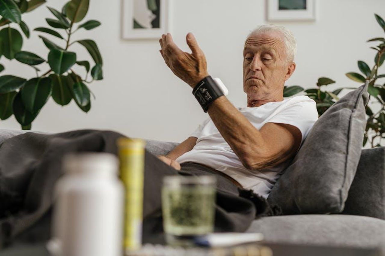 Source: SHVETS production - pexels - Elderly man checks his blood pressure using a wrist monitor in a comfortable living room setting.