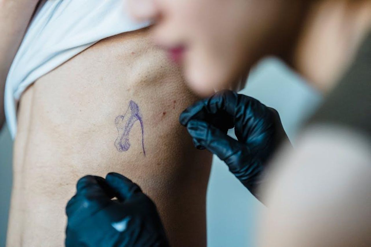 Source: Michael Burrows - pexels - Close-up of a tattoo artist applying a stencil design on a client's ribs during a tattoo session.