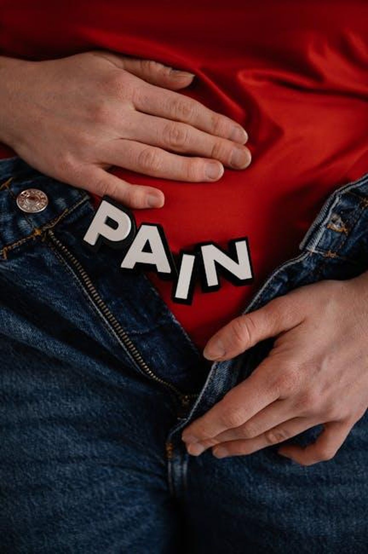 Source: SHVETS production - pexels - Close-up of a person in jeans holding their stomach with 'PAIN' text overlay.