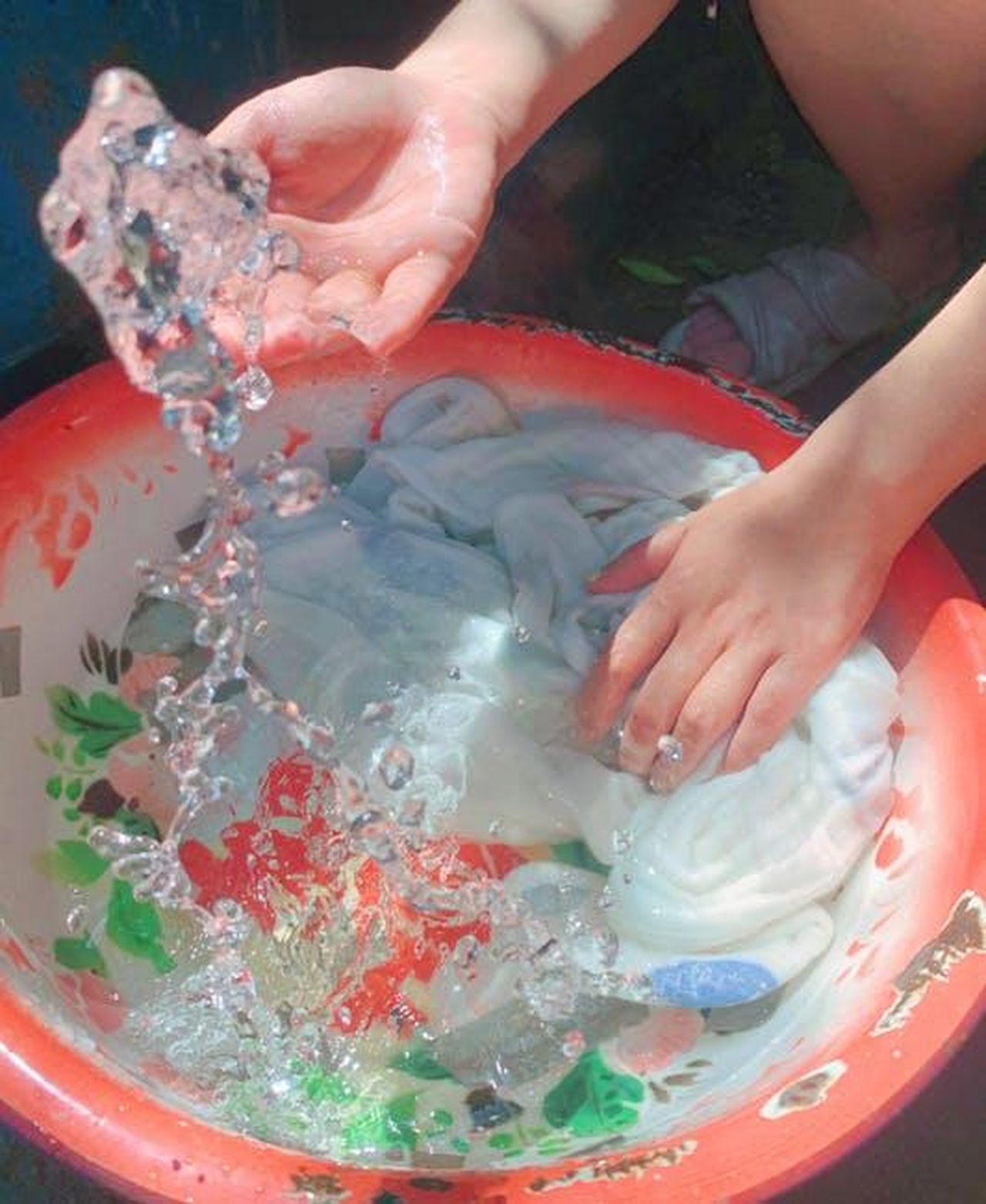 Source: 卜 兰 - pexels - Close-up of hands washing clothes in a red basin outdoors. Sunny day.