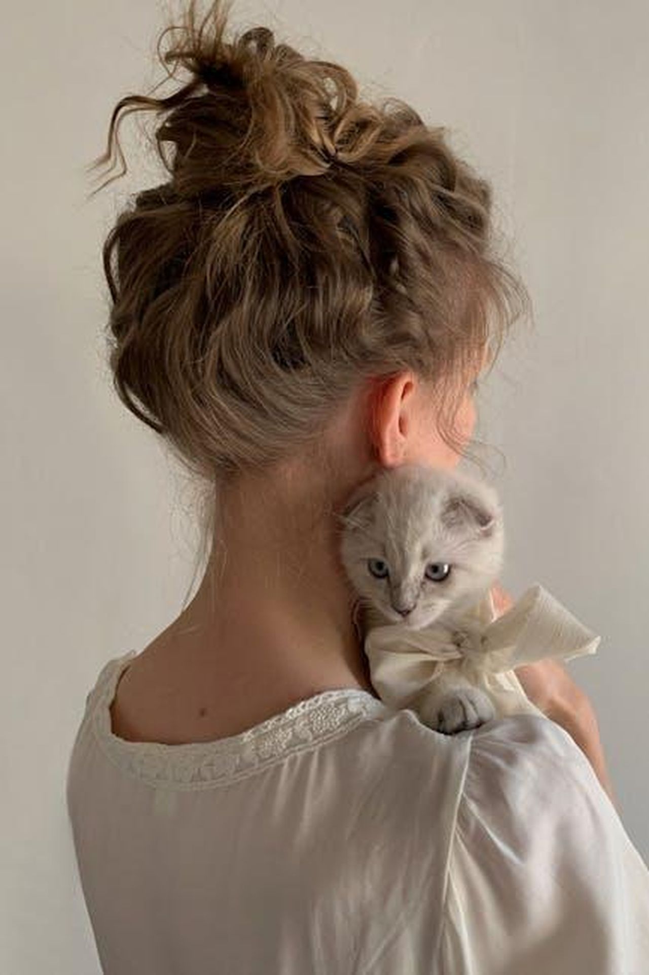 Source: Eugenia Remark - pexels - Young woman in Paris holds a kitten with a bow, showing a gentle bond.