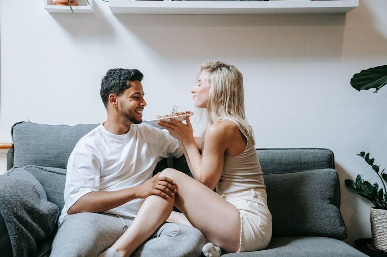 Source: Anna Pou - pexels - Romantic moment of a couple sharing food on a cozy couch at home.