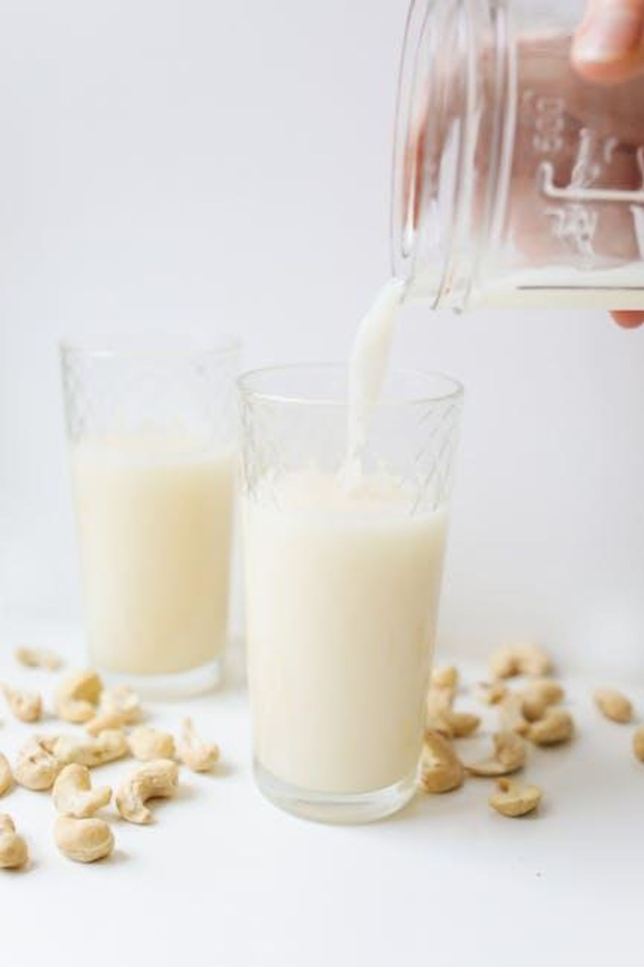 Source: Polina Tankilevitch - pexels - Delicious cashew milk being poured into a glass surrounded by cashews, showcasing refreshing plant-based nutrition.