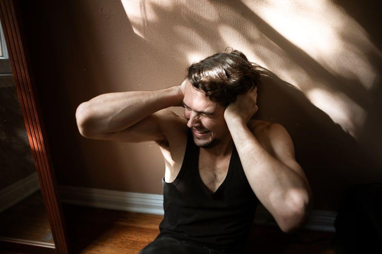 Source: RDNE Stock project - pexels - A man sitting on the floor indoors, showing signs of stress by covering his ears.
